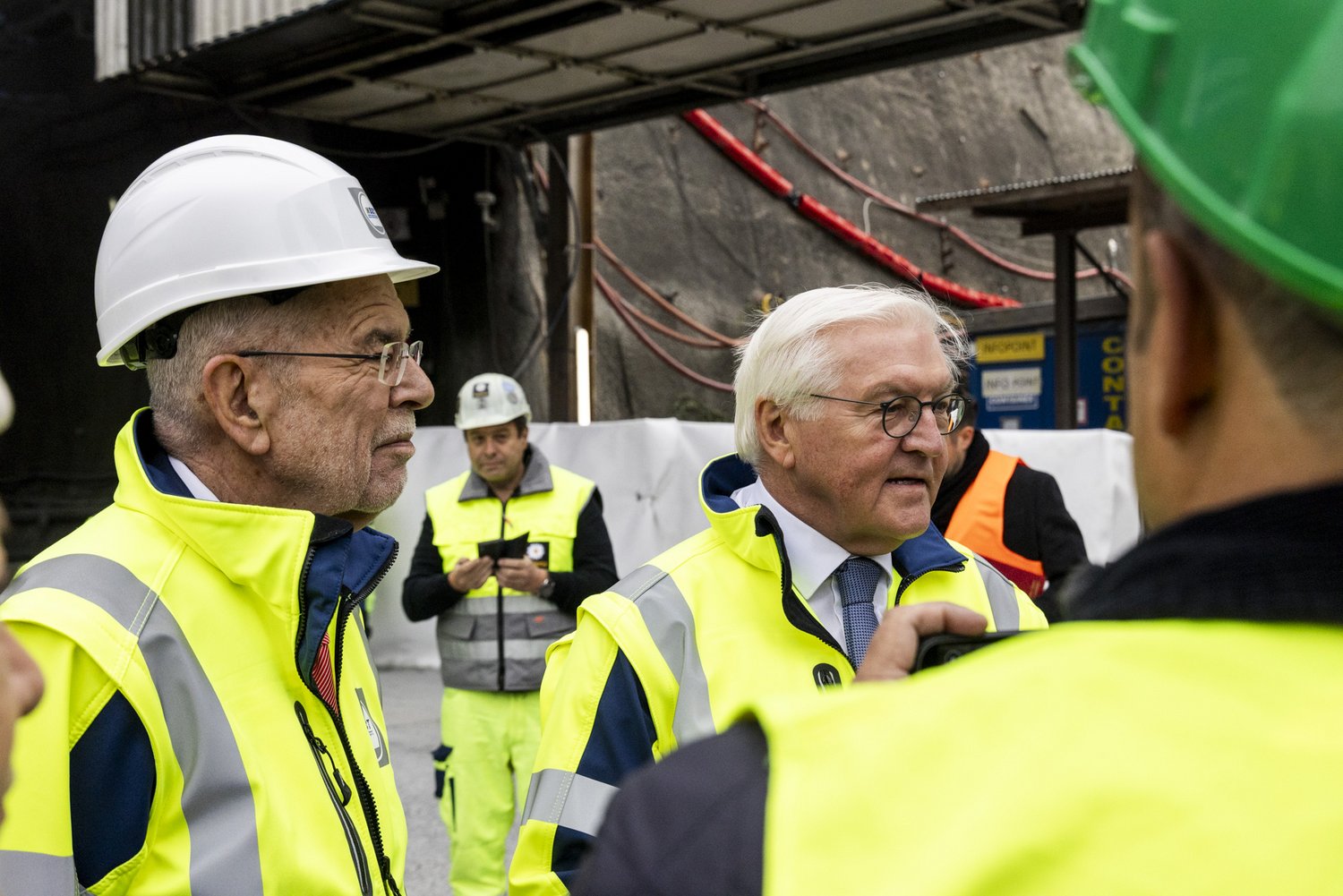 Österreichs Bundespräsident Van der Bellen und Deutschlands Bundespräsident Steinmeier vor dem Tunnelportal Ahrental. Beide tragen Schutzausrüstung. Um sie herum stehen weitere Teilnehmende der Delegation.