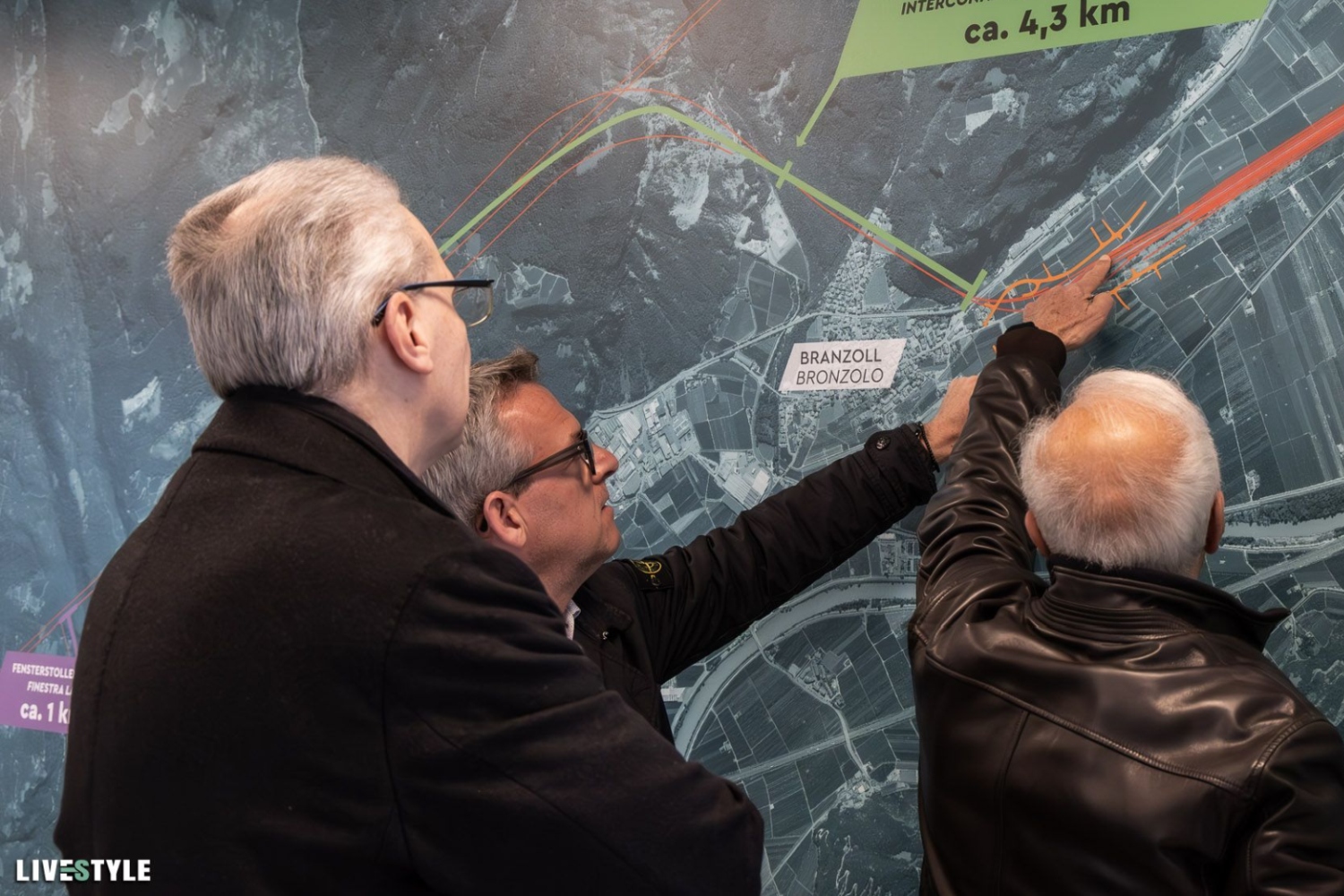 Eindrücke von der Eröffnung des Infopoints in Branzoll. Drei Besucher informieren sich an einer Karte über die Eisenbahnumfahrung von Bozen, von der auch der Ort Branzoll (italienisch: Bronzolo) berührt ist.